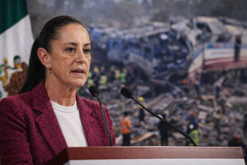Claudia Sheinbaum durante la conferencia mañanera, con imagen desenfocada del accidente del Tren Interoceánico al fondo.